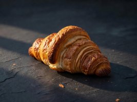 A flaky croissant on a dark slate background catching the morning light